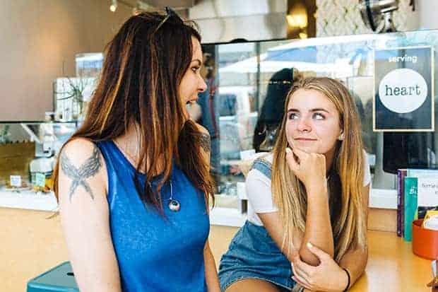 A woman in a blue sleeveless shirt and a girl in a blue jean overall dress and white t-shirt are sitting in a cafe. 