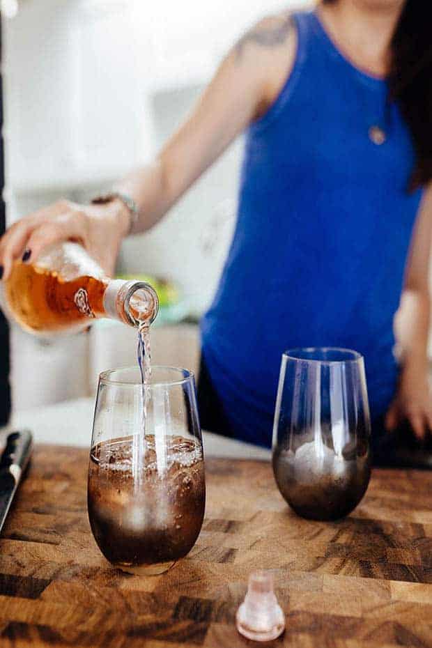 A woman pouring rosé into a stemless wineglass.