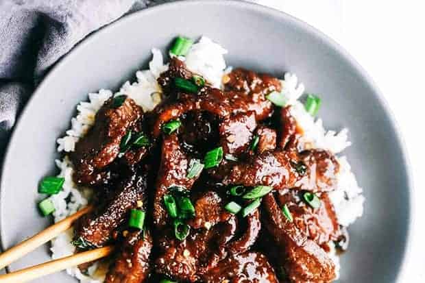 A gray bowl is filled with white rice and topped with Mongolian beef and scallions.