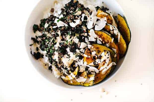 A white bowl on a white background. The bowl is filled with coconut kale, black lentils, roasted delicata squash and drizzled with dressing.