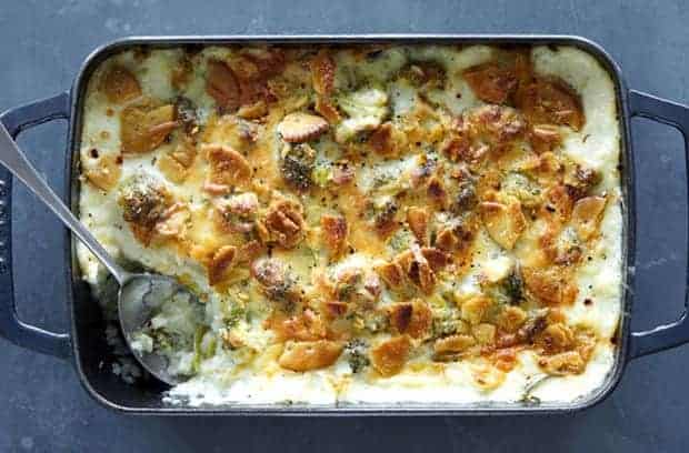 A baking rectangular baking dish full of cheesy broccoli rice casserole is sitting on top of a table top. There are crushed crackers on top of the casserole.