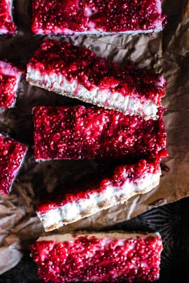 5 rectangular bars with a nut flour crust, coconut butter layer, and a raspberry chia jam layer. The bars are laid out on a piece of brown parchment.