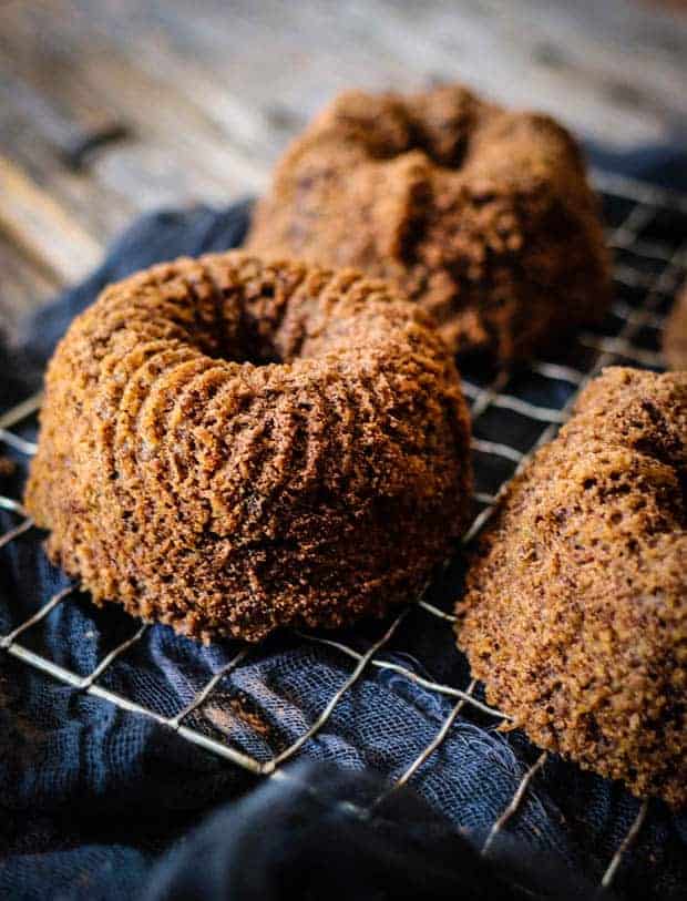 3 mini bundt cakes on a mesh cooling rack sits over a black linen cloth.