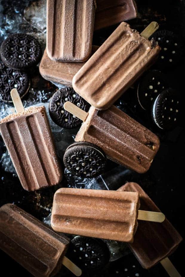 7 fudgesicles are scattered across a pan that has ice and chocolate sandwich cookies on it