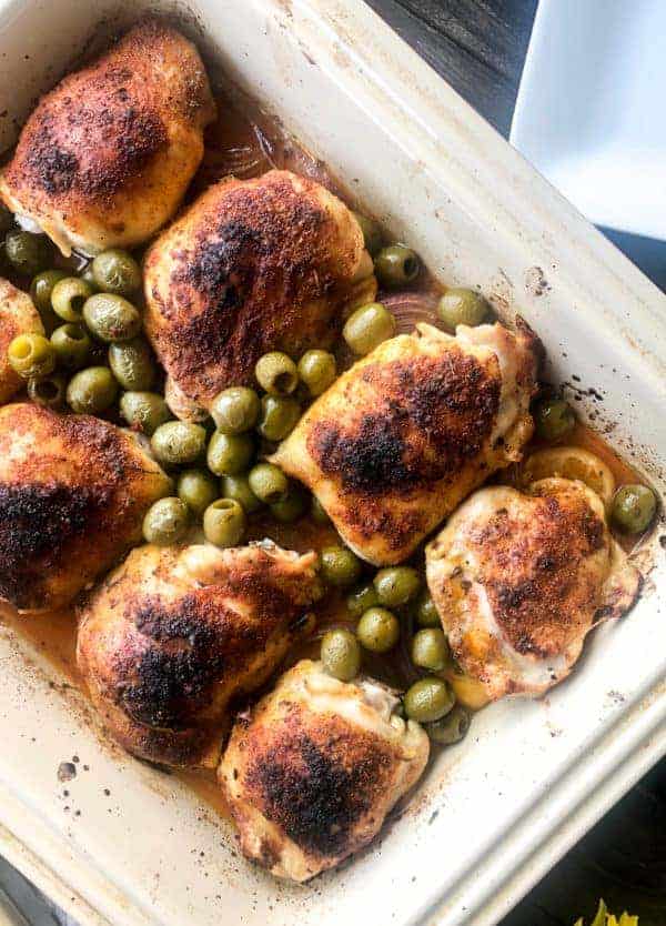 Golden brown chicken thighs in a pan wit their roasting juices and green olives