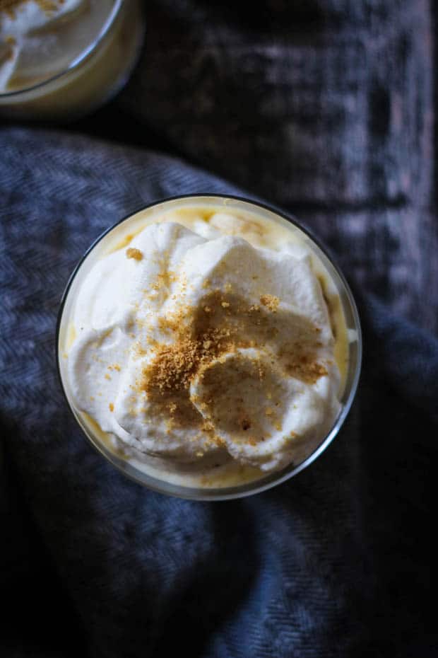 Top down image of a banana cream pie pudding cup. A mound of fluffy white whipped cream topped with ginger cookie crumb sprinkles. 