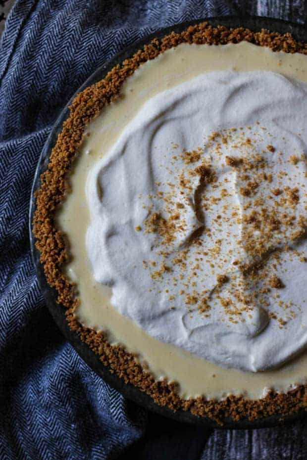 Close up of banana cream pie with ginger cookie crumb crust. Lots of swirly whipped cream on top and cookie crumb sprinkles.