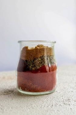 A jar of homemade taco spice seasoning before it is shaken up to mix. The layers of spices look like sand art.