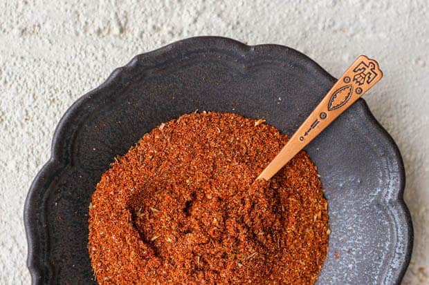 A black bowl of red taco seasoning with a small copper spoon dipped into it.