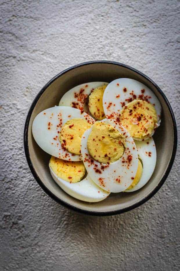 A brown and white bowl of halved hard boiled eggs sprinkled with red pepper flakes. 