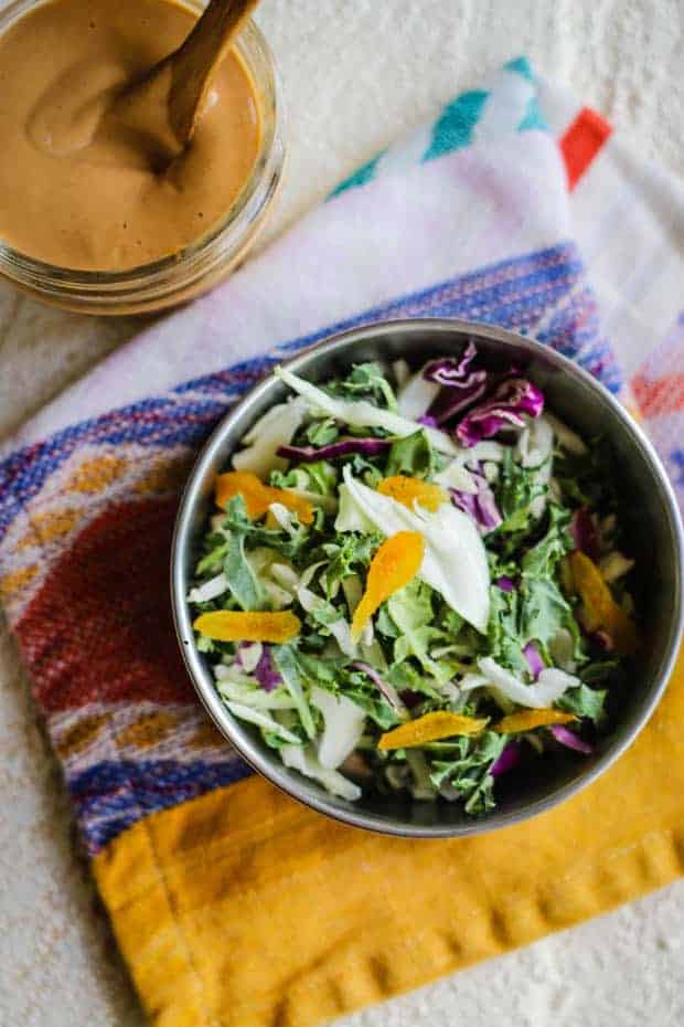 A bowl of colorful slaw with dried apricots is sitting on top of a colorful napkin