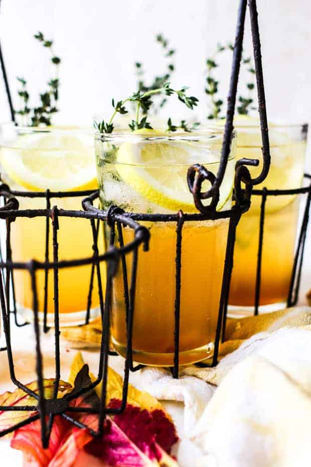 3 prepared cocktails that are golden in color with lot sof ice, lemon slices, and fresh thyme sprigs. The glasses are all in a vintage metal holder. 