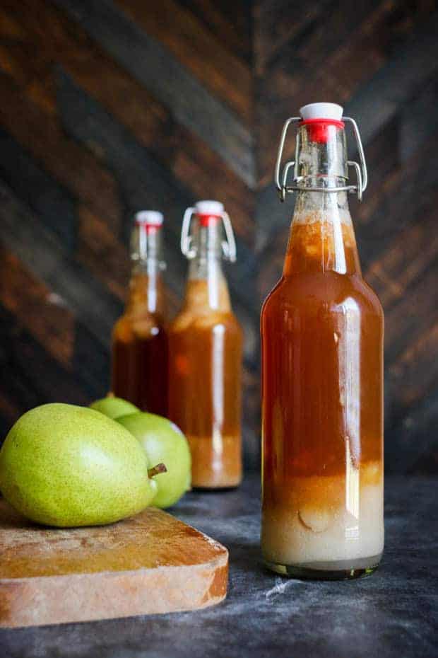 3 bottles of Chai Pear Kombucha on a table, one of the bottles is next to a green pear