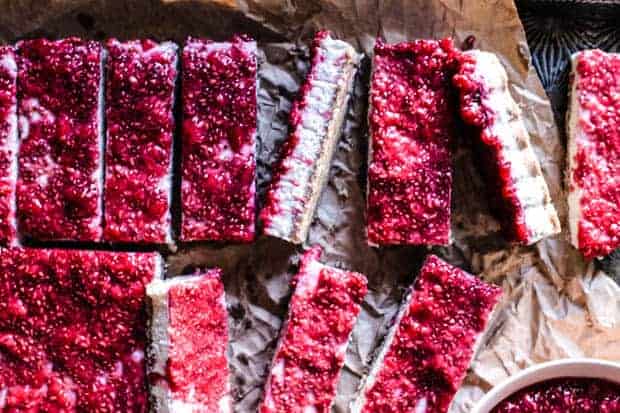 Close up of Paleo Raspberry coconut Bars turned different ways on a tray so you can see the crust, the white coconut filling, and teh red raspberry topping.