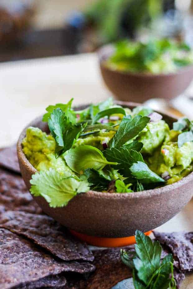 A bowl of guacamole topped with fresh basil, cilantro, and parsley leaves, fennel fronds and tarragon.