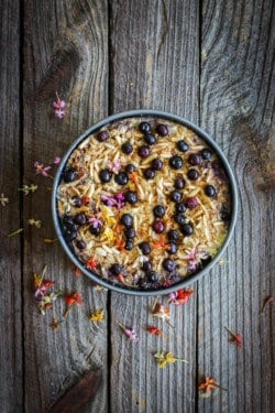 A round pan of blueberry banana baked oatmeal. The oatmeal is scattered with juice roasted berries and slivered toasted almonds.