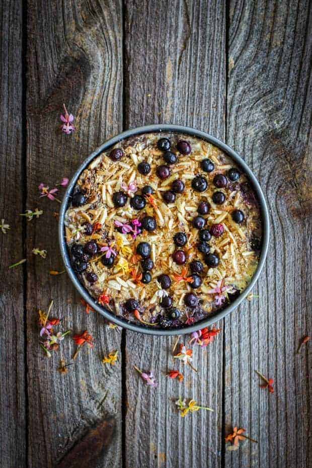 A round pan of blueberry banana baked oatmeal. The oatmeal is scattered with juice roasted berries and slivered toasted almonds. 