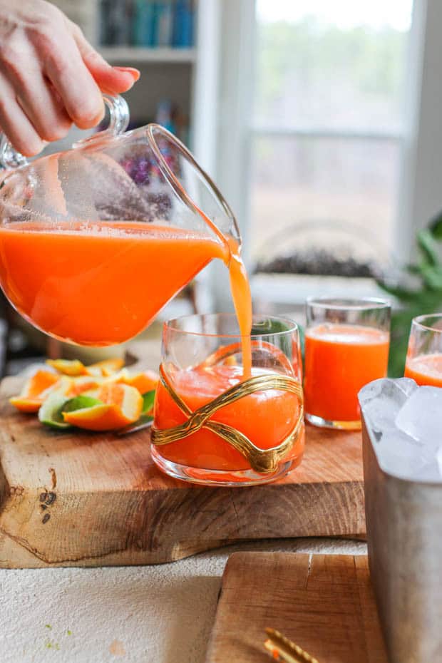 Immune boost juice being poured from a pitcher into a glass next to a metal dish of ice.