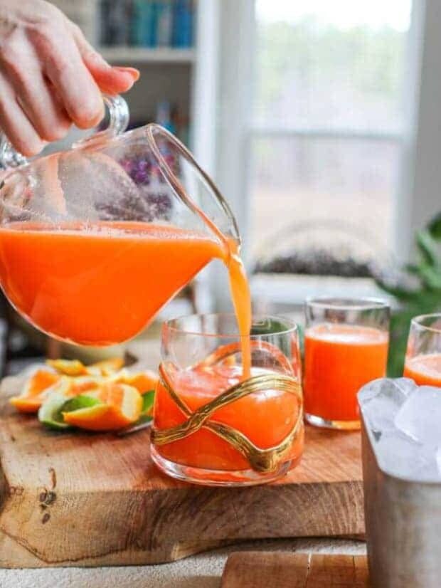 Immune boost juice being poured from a pitcher into a glass next to a metal dish of ice.