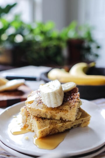 A plate with 2 slices of roasted banana chai sheet pan pancakes topped with maple syrup and fresh banana slices.