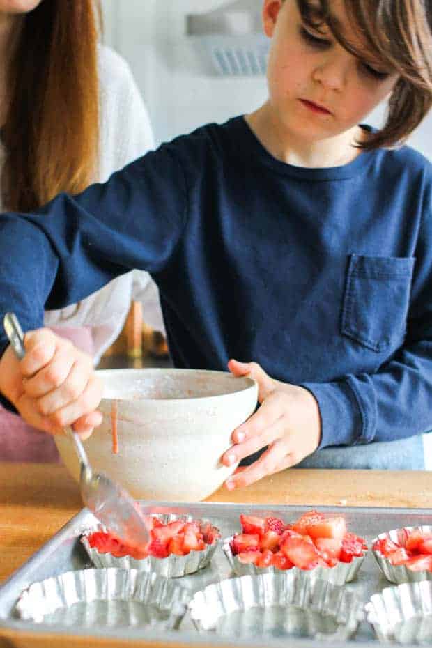 A boy scooping strawberries into mini baking pans.