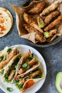 A platter full of Crunchy Gluten Free Avocado Taco s is next to a serving dish that is full of crispy golden avocado wedges