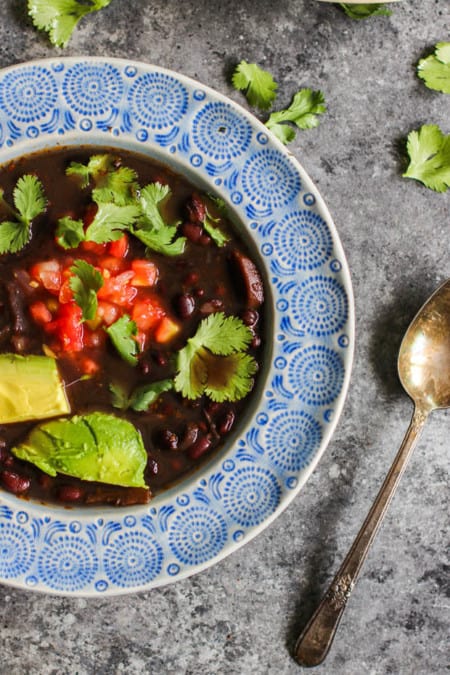 A close up of a bowl of Instant Pot Black Bean Soup topped with salsa, avocado, and cilantro leaves