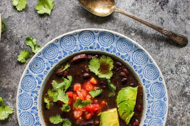 Instant Pot Black Bean Soup in a bowl with fresh avocado, pico red gallo, and cilantro leaves