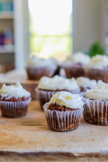 8 Easy Gluten Free Carrot Cake Muffins on a wooden table in front of a window.