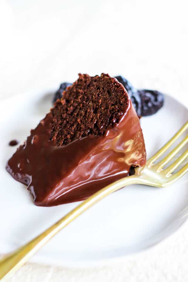 A slice of Chocolate Covered Prune Fudge Cake on a plate with dried prunes