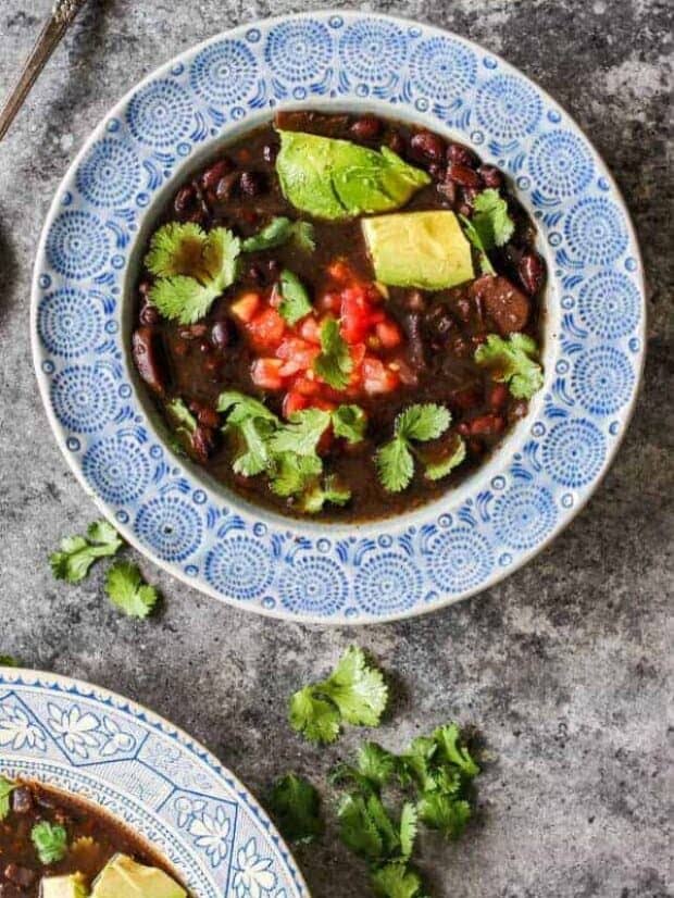 Bowls of Instant Pot Black Bean Soup topped with avocado, cilantro, and pico de gallo