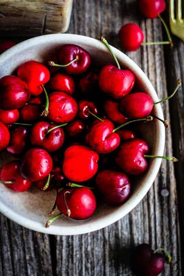 A bowl of fresh cherries on a wood table
