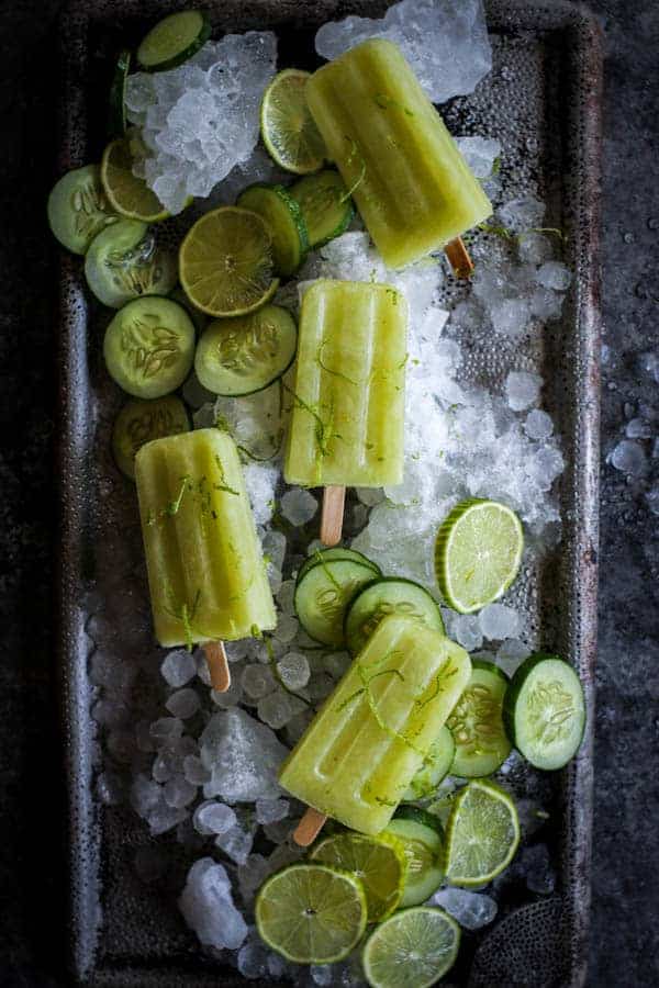 4 Cucumber Limeade Popsicles on a platter of shaved ice with cucumber slices and lime zest
