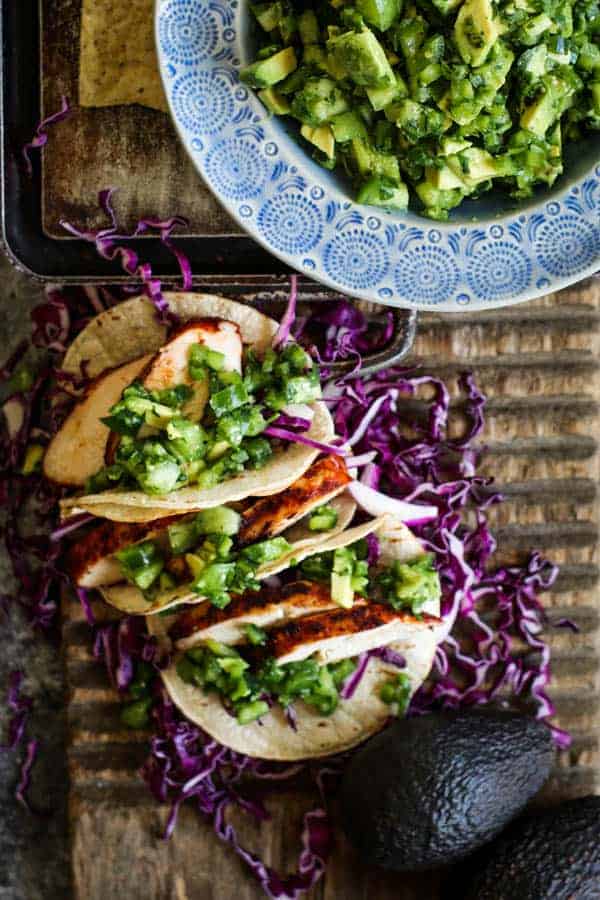 A trio of Easy Grilled Enchilada Chicken tacos next to a bowl of f green pico de gallo