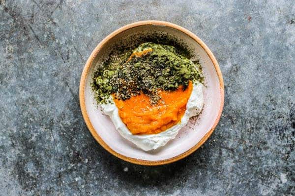 A Pumpkin and Yogurt Bowl for Dogs on a metal table top. It is layered with yogurt, pumpkin puree, vitamin powder, and herbs.