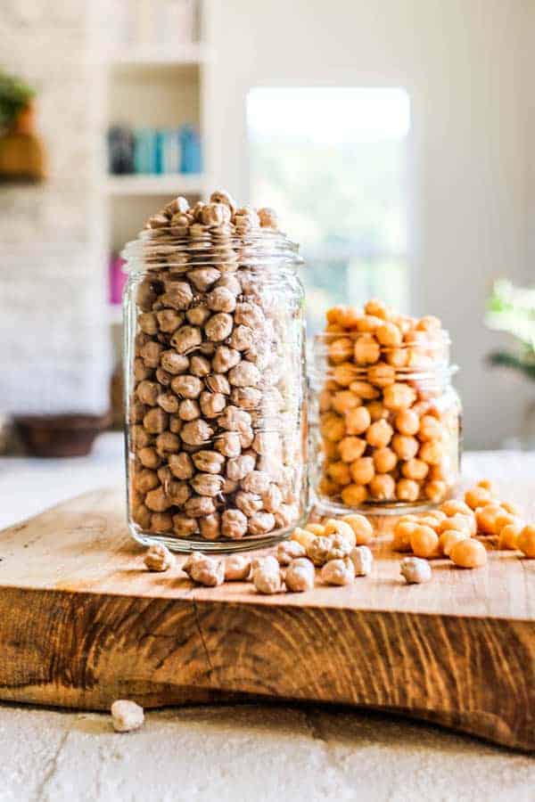 2 jars of chickpeas sitting on a table top - one has dried chickpeas and one has canned.