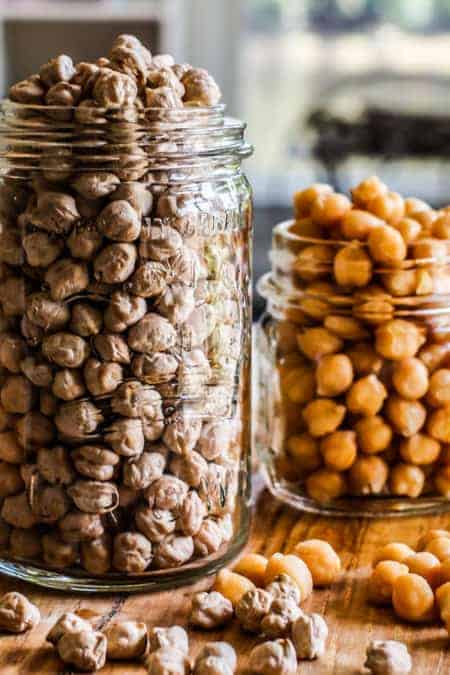 A close up of 2 glass jars filled with chickpeas. One jar has dried chickpeas and one has canned chickpeas