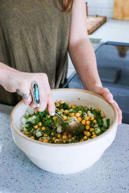 A bowl of soaked chickpeas and herbs being stirred together