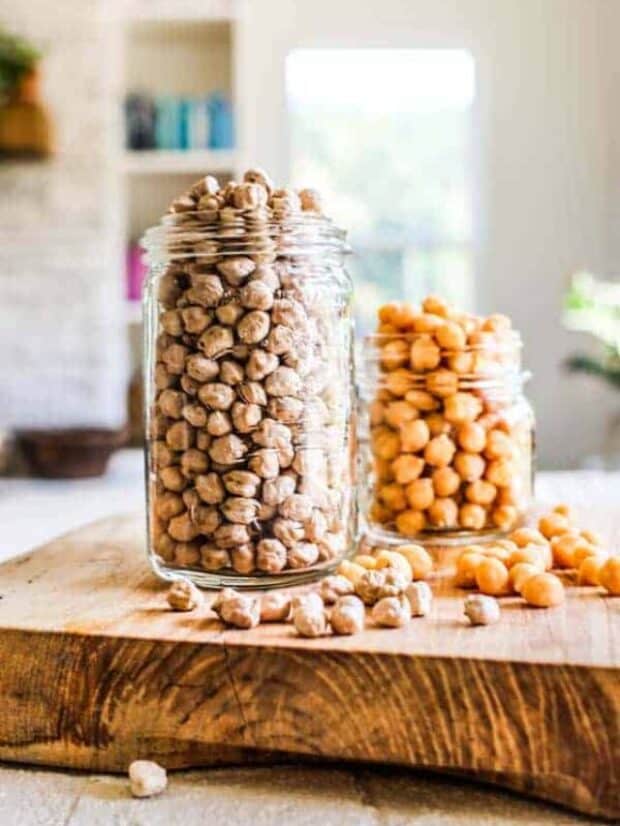 2 jars of chickpeas sitting on a table top - one has dried chickpeas and one has canned.
