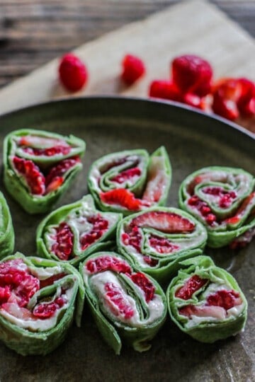 A plate of Easy Fresh Berries and Cream Roll Ups next to fresh raspberries