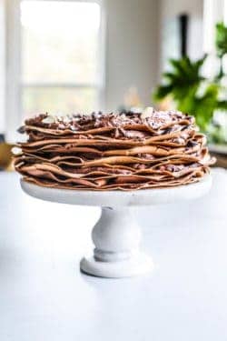 A chocolate crepe cake on a white cake stand