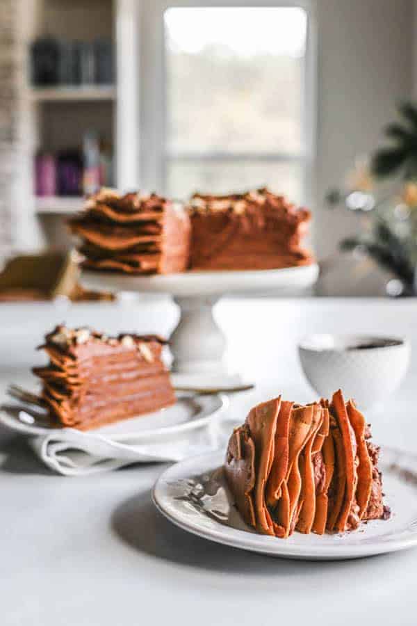 A chocolate crepe cake on a cake stand with 2 slices on plates