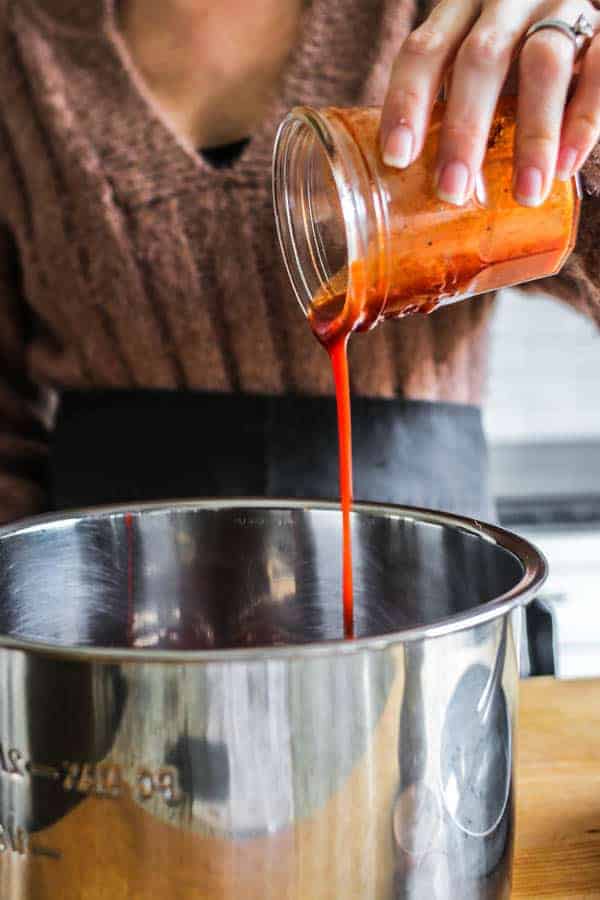 A woman pouring enchilada sauce into an Instant Pot 