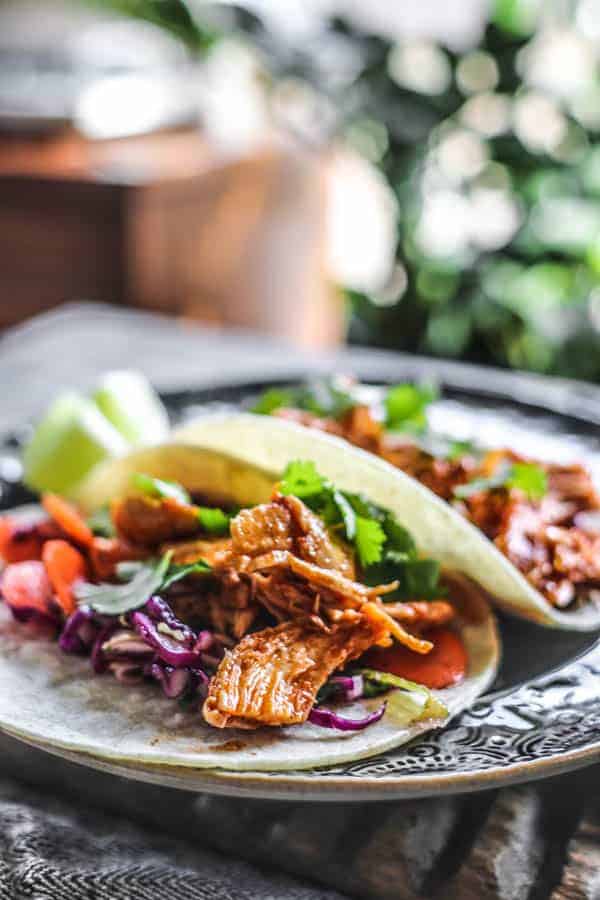 Two tacos on a plate with shredded Mexican chicken recipe , a colorful slaw, and cilantro on white corn tortillas