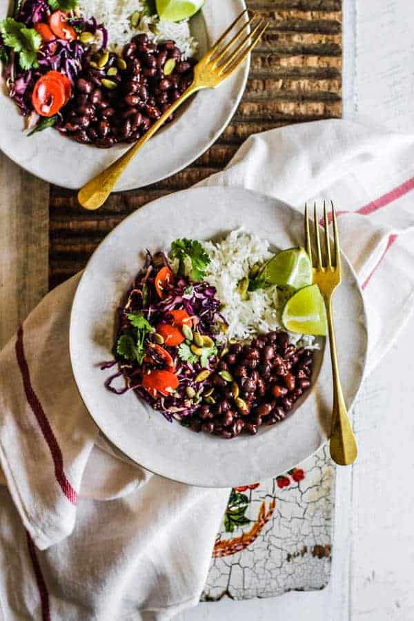 Two vegetarian burrito bowls with black beans, rice, spicy colorful slaw, and lime wedges