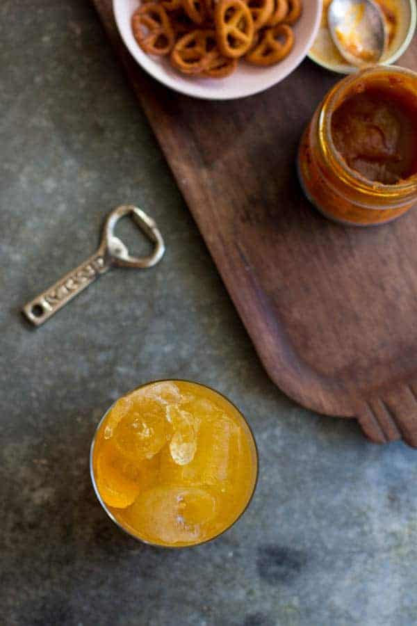 A Pumpkin Butter Dark and Stormy, battle opener, and bowl of pretzels on a table top. 