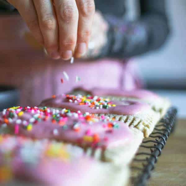 A woman adding colorful sprinkles on tp of freshly iced homemade pop tarts