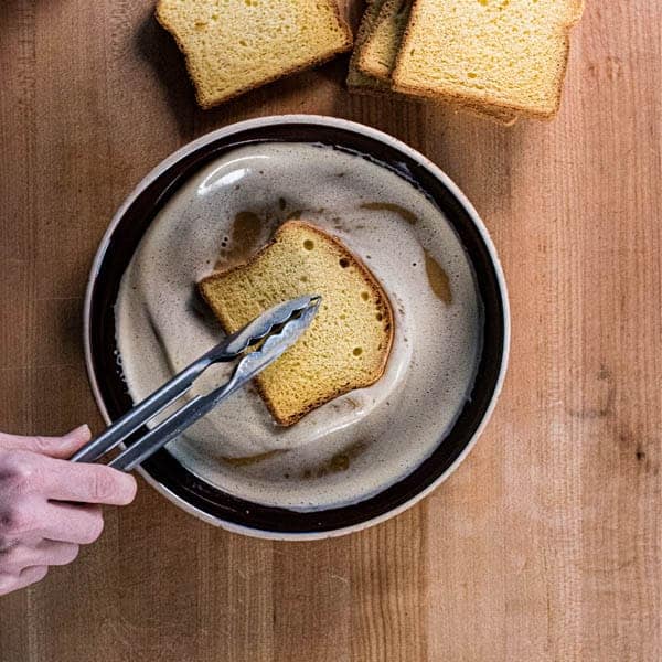 A piece of brioche being dipped into the custard for the perfect french toast recipe