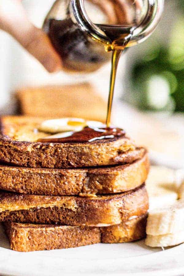 A stack of French toast up close with butter on top and maple syrup being poured over it.