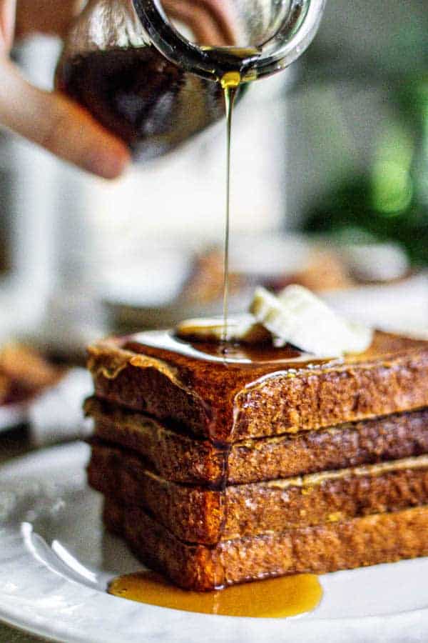 A stack of French toast being drizzled with warm maple syrup